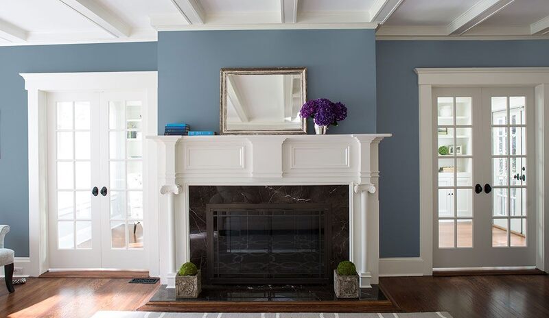 A white fireplace and mantel in a blue living room with windowed double doors.