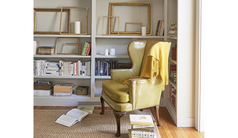 A study with greige-painted walls features alcove bookcases with books and frames, a cozy chair