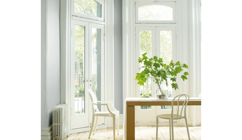A gray dining room features a wooden table, two chairs, leafy branches in a vase, and French doors.