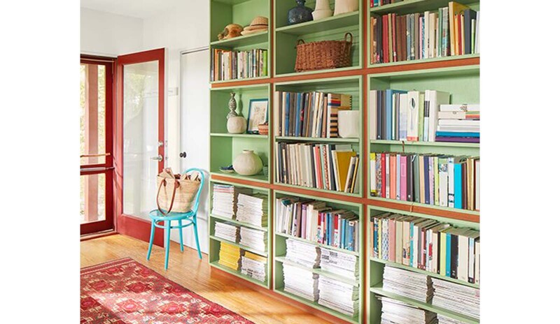A sunlight entryway with green-painted bookshelves, wood floors and red-painted front door.