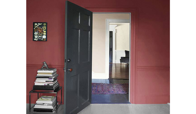 A pomegranate-colored wall with an open dark gray-painted door and table with books.