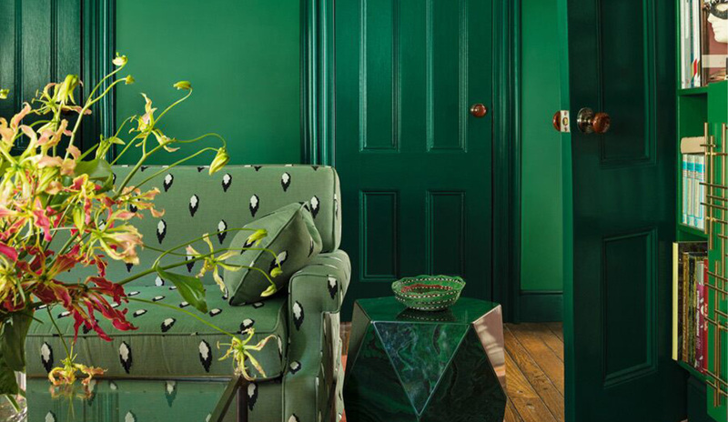 A green-painted living room with green-printed couch, stone and bookshelves matching the walls. 