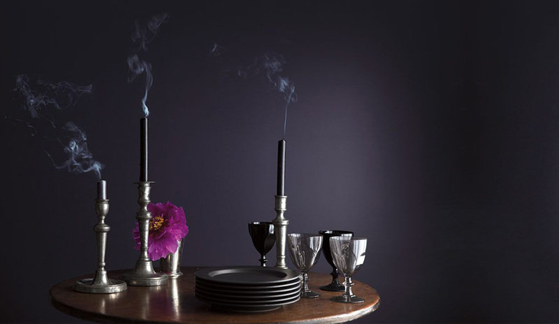 An oval wooden table with just blown-out candles and small plates against a deep purple wall.