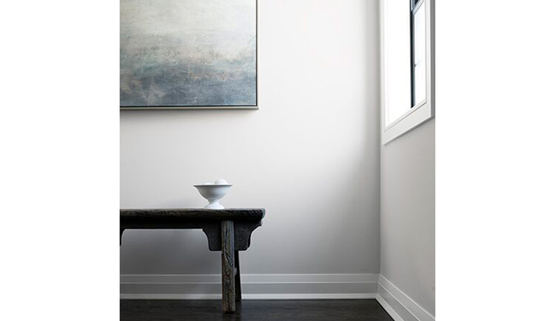Un pasillo con paredes y molduras blancas, un banco de madera negro y arte contemporáneo.
