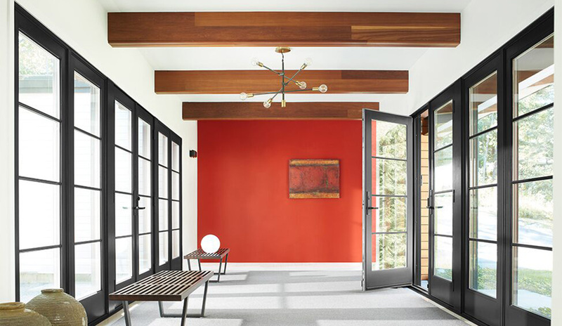 A white-painted hallway with a red accent wall, wood beam ceiling, black-trim windows and door.