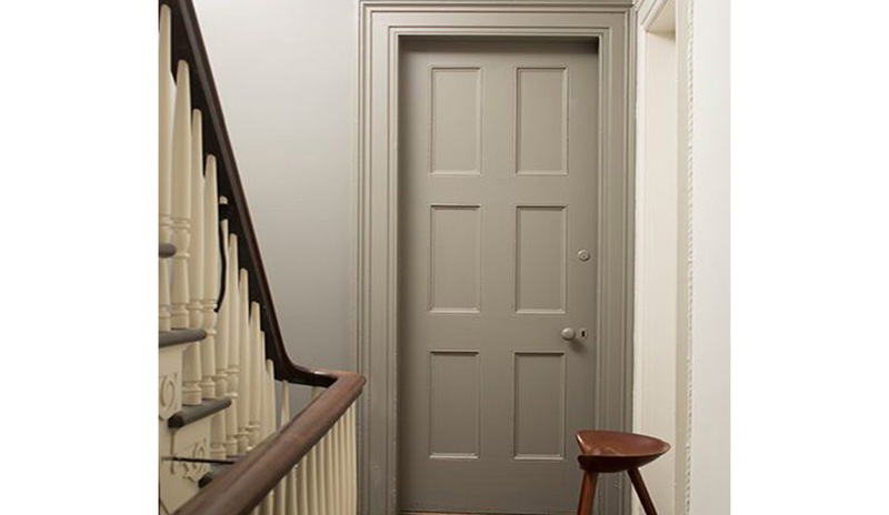 A hallway painted in neutrals with a wooden floor, a gray-painted door