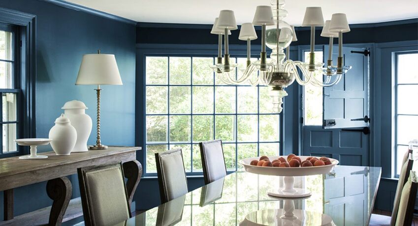An all-blue painted dining room with chandelier and French door.