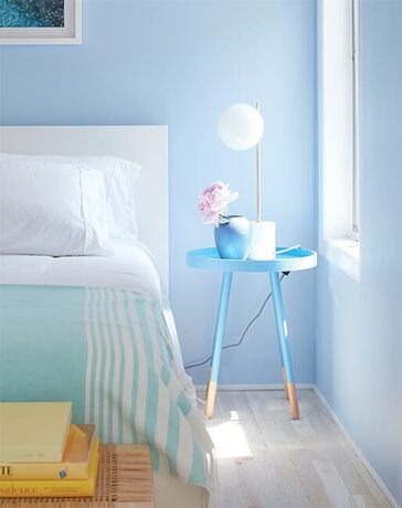 Vibrant blue bedroom with bright blue side table and white bed.