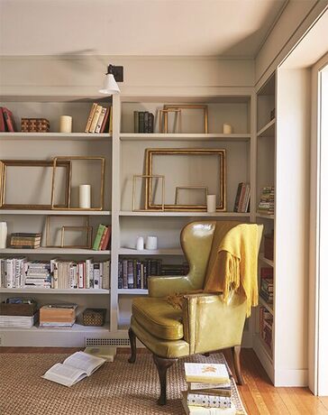 A study with greige-painted walls features alcove bookcases with books and frames and cozy chair.