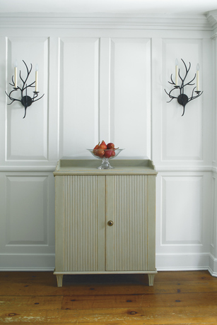 Panelled gray-painted walls frame a chest centered between candle sconces.