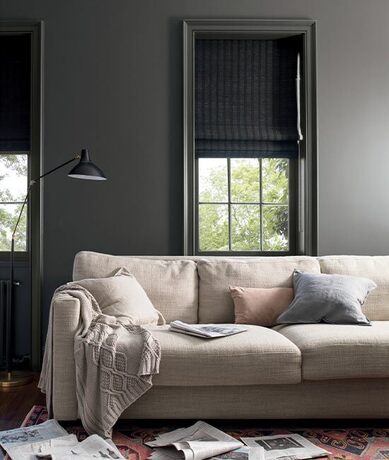 Dark gray living room with matching window trim featuring a tan couch with three pillows.