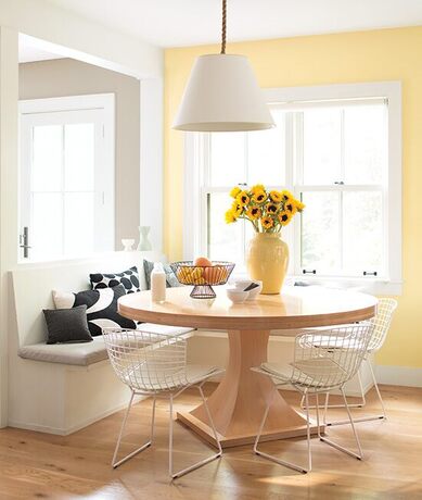 Sunny dining room, yellow accent wall, white details, wooden table, wire chairs, greige wall