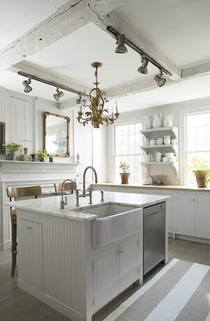 White kitchen with open shelves, island, sink, mantel, lights, and chandelier.