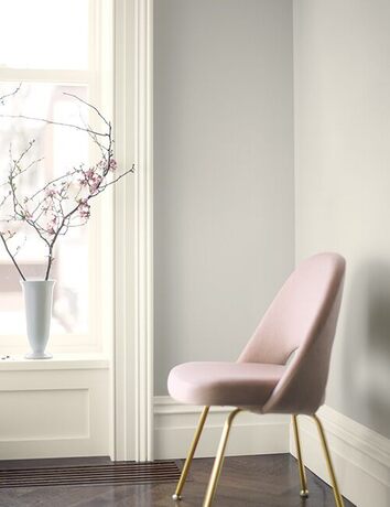 A pink chair against light gray walls with off-white trim, a vase on the windowsill.