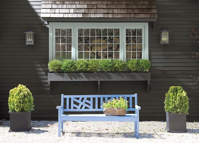 Black house, pale-blue trim, baby blue bench, shrubs, potted plant.