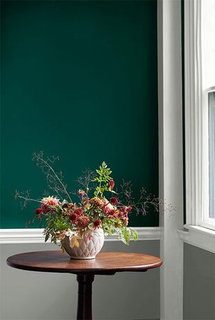 A hunter green wall with white trim and gray wainscoting frames a round wooden table.