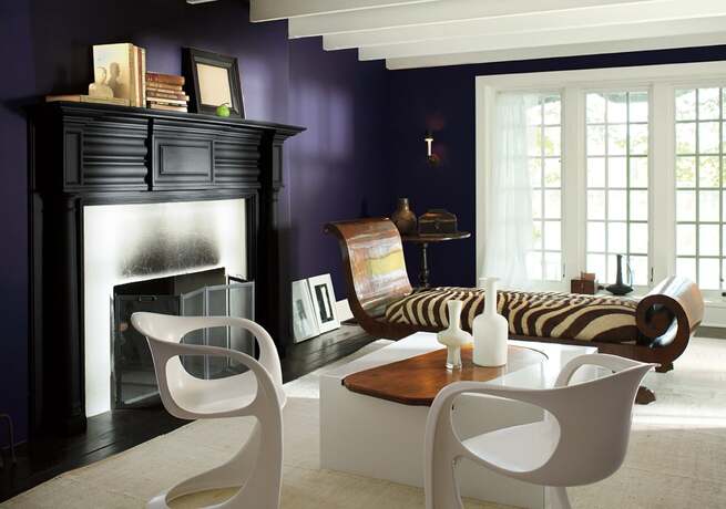 Una sala de estar con paredes de color violeta intenso, una chimenea con repisa pintada de negro.