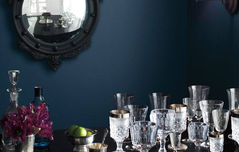 Una pared de comedor pintada de azul oscuro enmarca copas ornamentadas sobre una mesa.