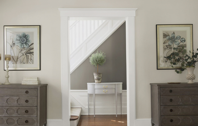 A gray and neutral hallway leads to a white staircase.