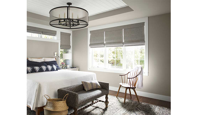 A well-lit, neutral bedroom with large white bed and blue pillows, wooden spindle-back chair.