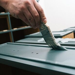 Primer is applied to the surface of a cabinet in a room with white walls.