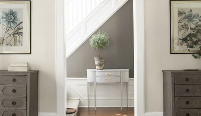 A gray and neutral hallway leads to a white staircase.