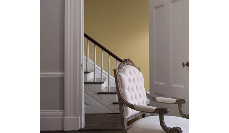 A living room in light gray features a door opening to a yellow-painted foyer.