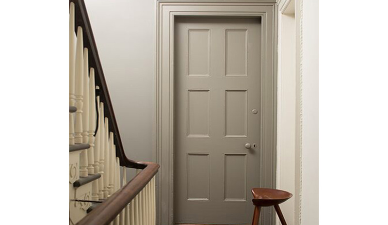 A hallway painted in neutrals with a wooden floor, a gray-painted door A hallway painted in neutrals with a wooden floor, a gray-painted door