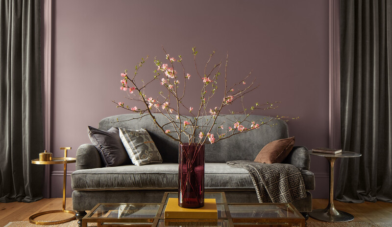 A purple living room has a gray couch, gold side tables, and a glass coffee table