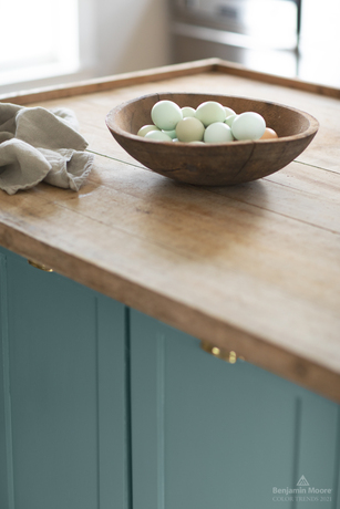 Una isla de cocina con encimera de madera y gabinetes pintados Aegean Teal 2136-40.