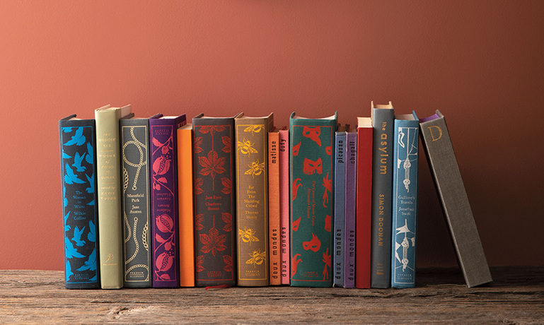 Libros en un estante debajo de un espejo colgante y pared pintada en Rosy Peach 2089-20.