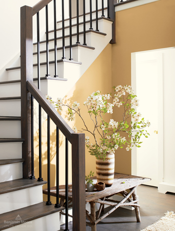 A staircase with wooden railings, white risers, and walls painted in Chestertown Buff HC-9.