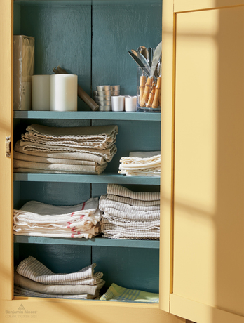 An open linen cabinet painted in Chestertown Buff HC-9 and Aegean Teal 2136-40.