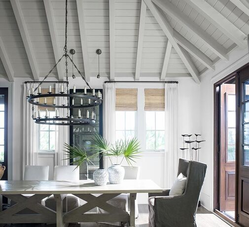 Un moderno comedor blanco con techo revestido de madera y un candelabro colgante a la luz de las vel