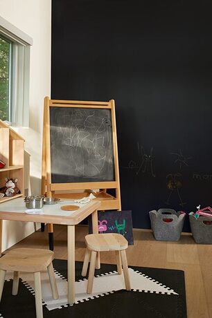 Zona de juego con pared de pizarra, caballete, mesa de dibujo, cubos de fieltro y estantes.