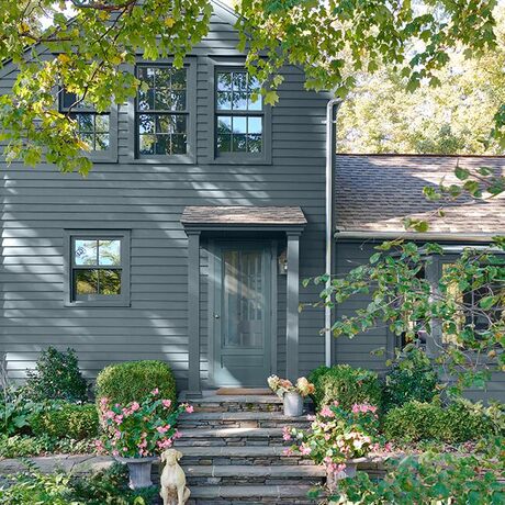 Una casa pintada de azul grisáceo muy bien sombreada, con puertas azules y un pintoresco sendero