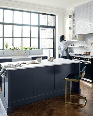 Una isla de cocina azul marino con encimeras de mármol blanco en una cocina abierta con ventanas