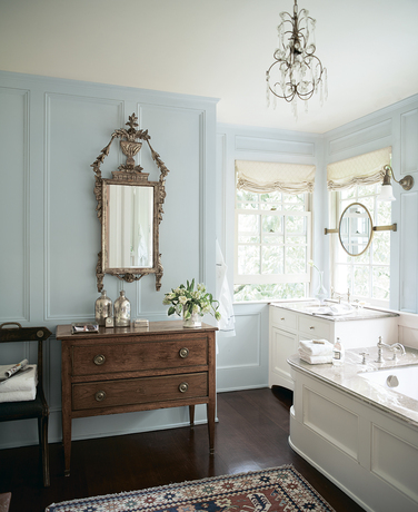 Un baño pintado de azul claro con espejo vintage y aparador.