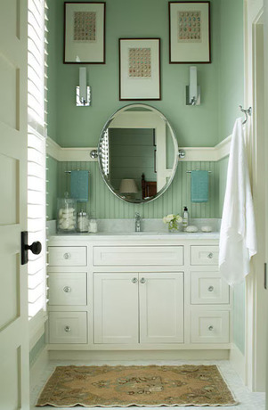 Seafoam green bathroom with circular mirror and three picture frames hanging above a white vanity.