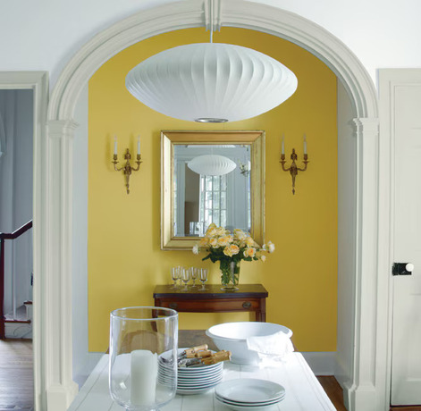 A dining room with a modern lamp, white farmhouse table and antique chair