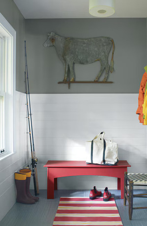 A mudroom with a cow illustration on a gray wall, red bench, striped rug, and white-tiled walls.