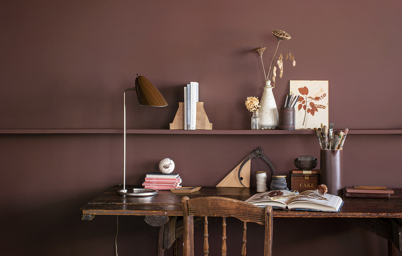 An office with brown-painted walls, a long wooden shelf, and a matching wooden desk and chair
