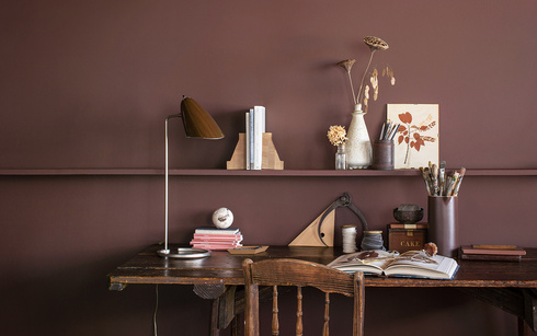 An office with brown-painted walls, a long wooden shelf, and a matching wooden desk and chair