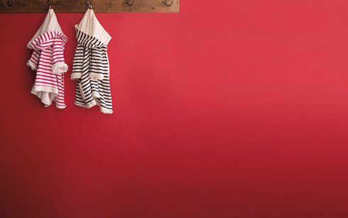 Red wall with a wooden plank coat rack, two striped children's robes, one in pink and one in black.