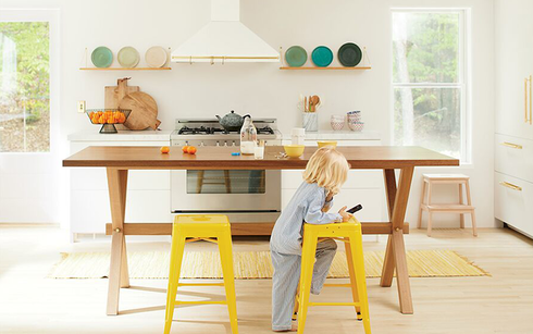 White kitchen with range hood, stove, and open shelves displaying colorful plates.