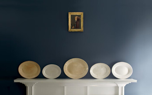 Una repisa de madera blanca presenta platos decorativos contra una pared azul.