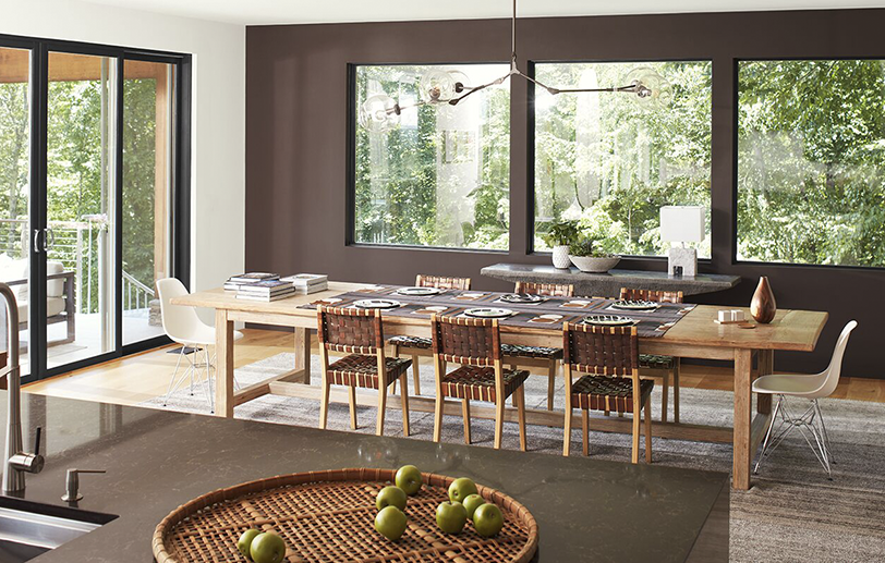 Comedor moderno con pared de acento marrón, techo blanco y puertas de vidrio, y una isla de granito 