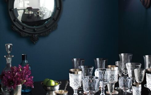 A dark blue-painted dining room wall frames ornate glasses on a table.