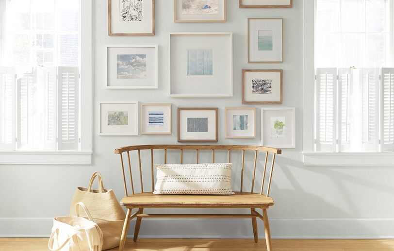 An off-white painted wall with a collection of framed art behind a wooden bench and shopping bags. An off-white painted wall with a collection of framed art behind a wooden bench and shopping bags.